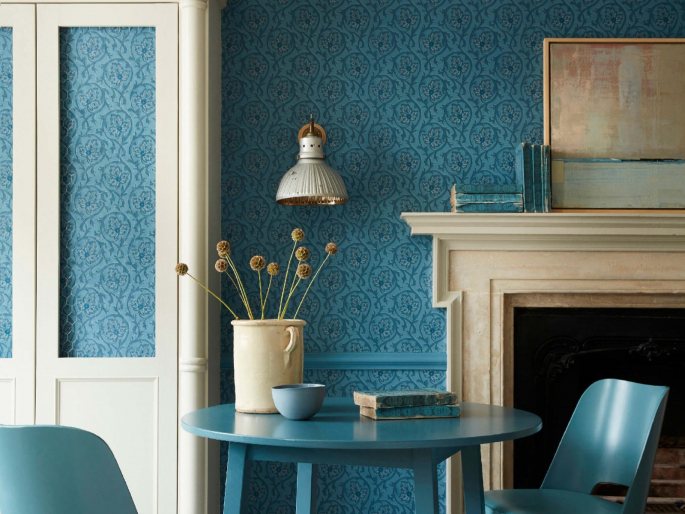 Blauw behang met sierlijke krullen Hoja - Air Force Blue van Little Greene toegepast in een woonkamer met grote schouw